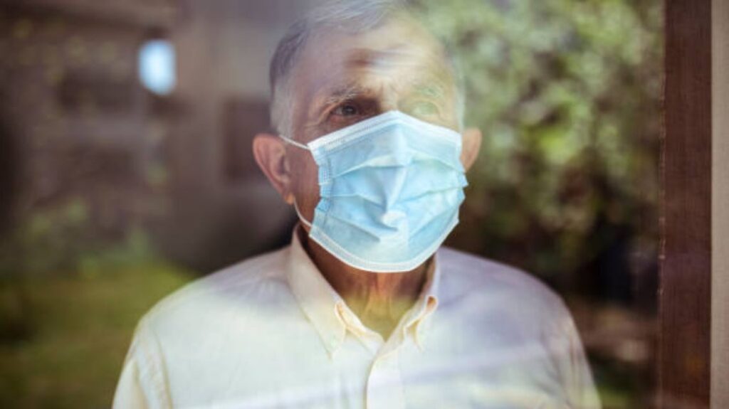 Senior man stays home because of Corona virus. He stands by the window and looks out at the garden